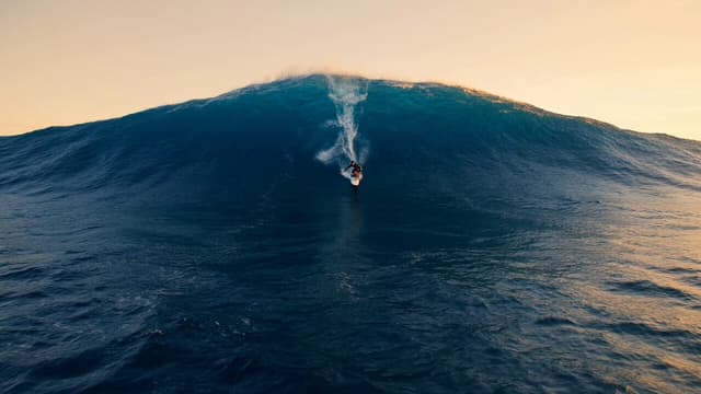 Grok Imagine Prompt - A professional surfer drops into a towering wave at sunset,
